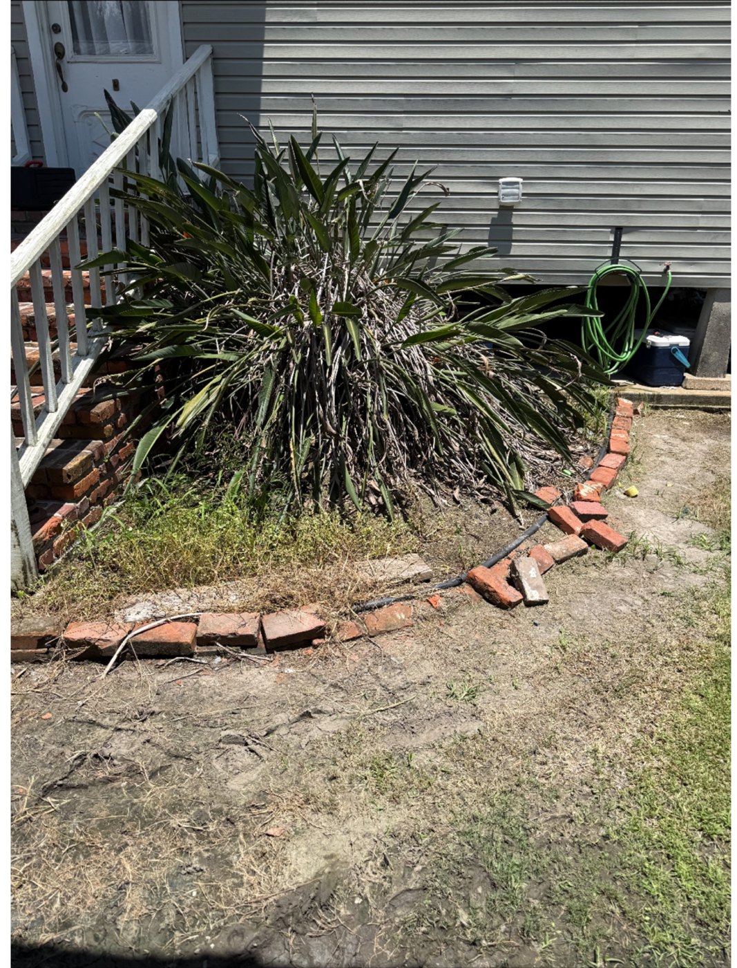 Before: an overgrown flowerbed beside porch steps with scattered loose bricks and bare dirt